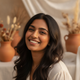 Smiling South Asian woman in her late 20s, portrait headshot, against a soft background of terracotta and white tones.