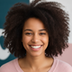 Portrait of a smiling young adult woman with medium brown skin and dark, curly hair, wearing a rose top.